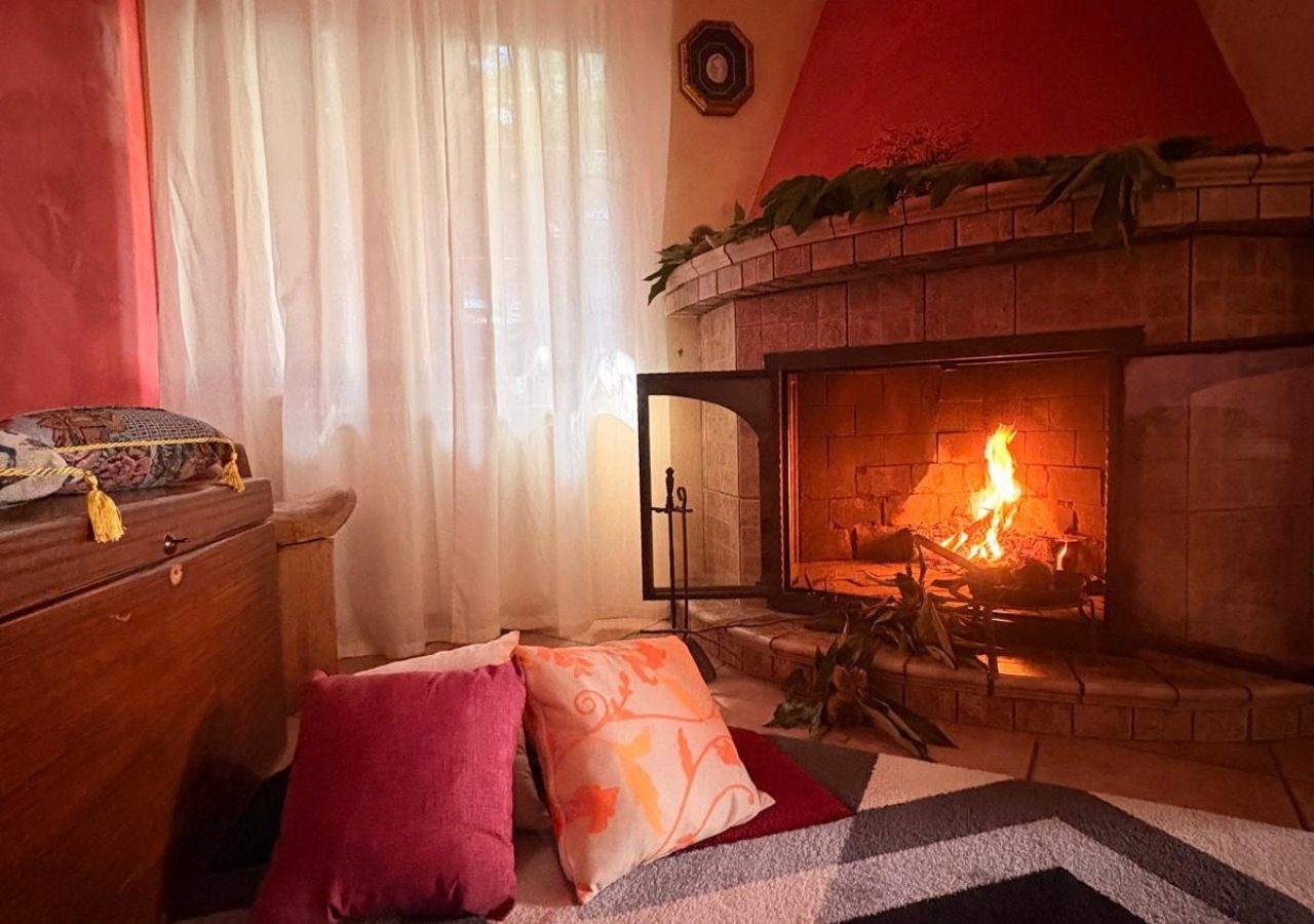 Il camino acceso nel soggiorno dello chalet, con cuscini e tappeto davanti al fuoco